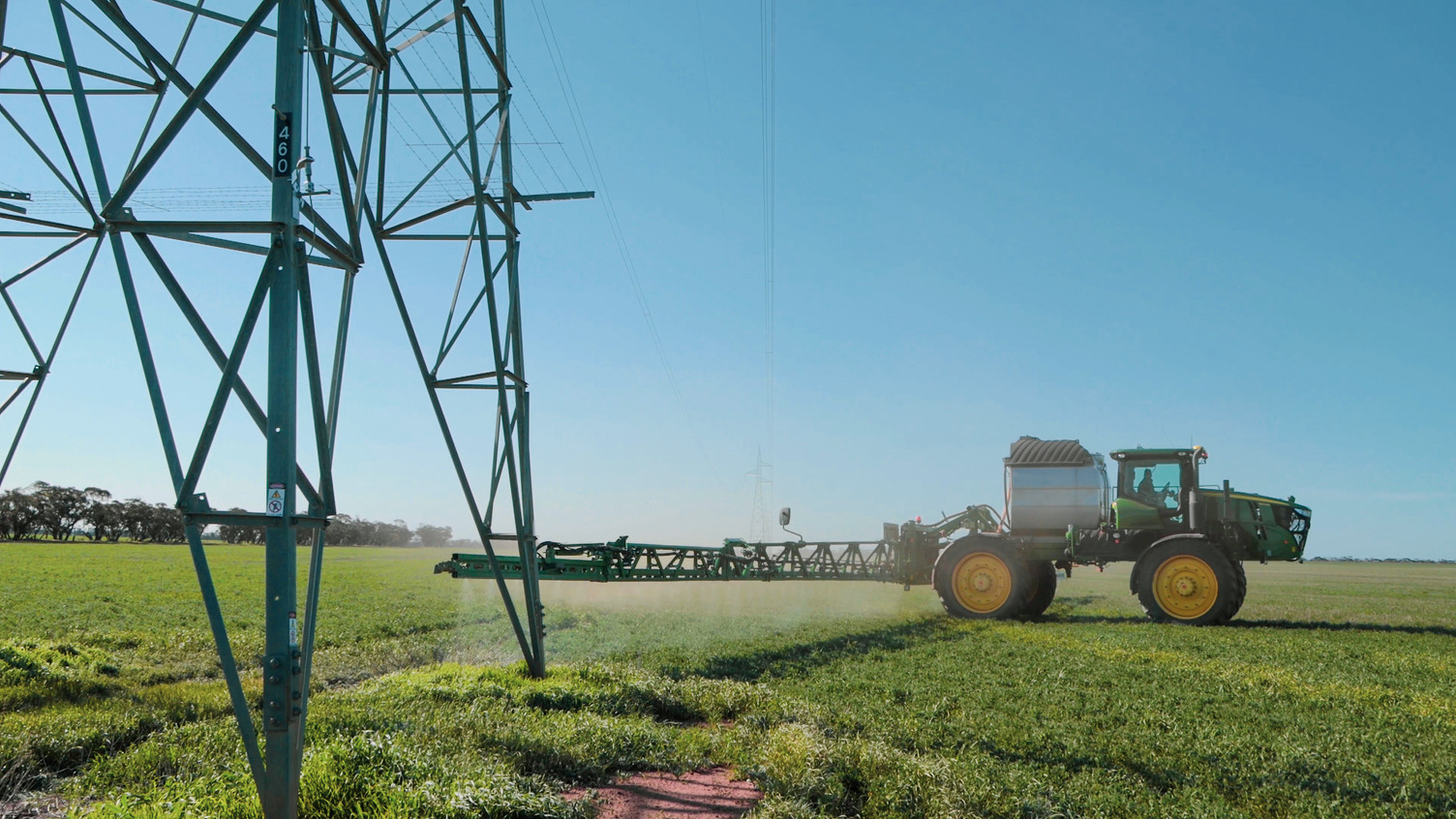 A farming machine working on crops near a transmission tower