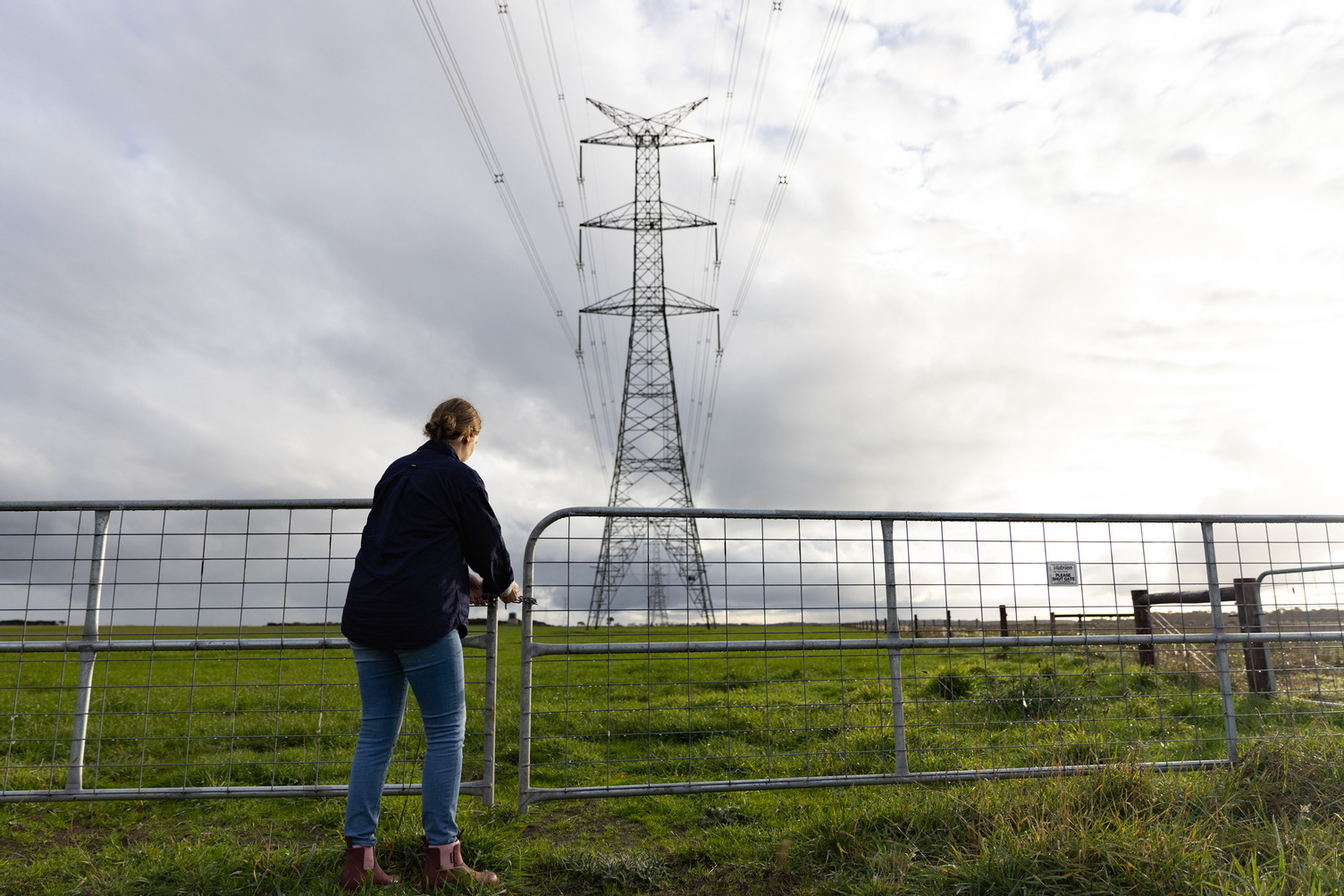 A woman opening a gate near a transmission tower