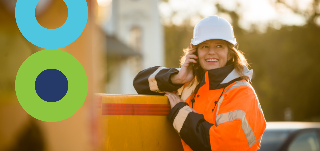 A woman working outside smiling and holding a phone