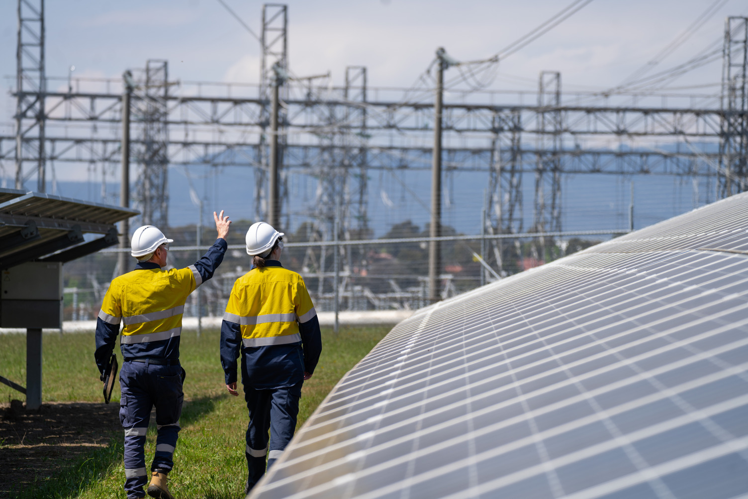 Two workers outside walking next to a large solar panel